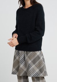 Pullover in maglia blu scuro con colletto a girocollo e polsini a costine, abbinato a una gonna scozzese nei toni beige, nero e bianco.