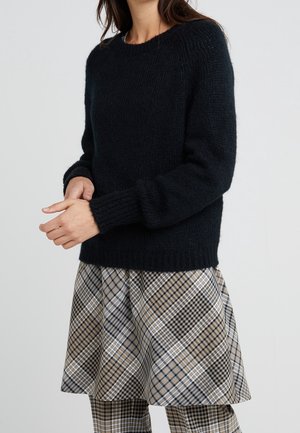 Mørk marineblå strikket sweater med rund hals og ribbede mansjetter, parret med et rutet skørt i beige, sort og hvide nuancer.