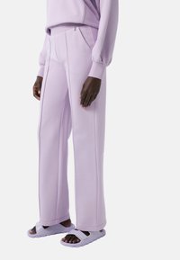 Licht lila sweatpants van zachte stof, met een ritszak, wijde benen en strakke lijnen. Gecombineerd met bijpassende slippers.