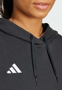Black hoodie with a soft texture, featuring a white Adidas logo and drawstrings. Close-up view of the neckline area.
