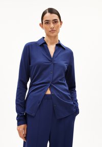 Marineblauw overhemd met lange mouwen, een kraag en een iets open voorkant. Heeft een zachte textuur en een comfortabele pasvorm, gecombineerd met bijpassende broeken.