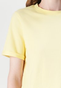 T-shirt jaune à manches courtes en mélange de coton doux ; présente un col rond et des manches retroussées pour une coupe décontractée.