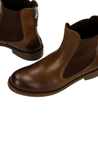 Stivaletti in pelle marrone con pannelli laterali elasticizzati, punta rotonda e una cerniera decorativa in argento sul retro. Texture liscia e suola resistente.