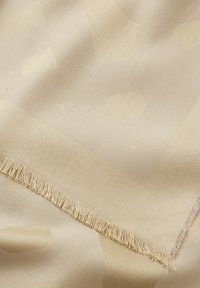 Bufanda beige con patrón de logo sutil, acabado texturizado y bordes con flecos, que crea un drapeado suave y una apariencia lisa.