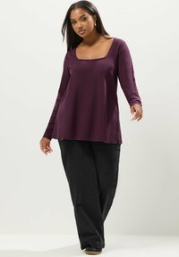 Top a maniche lunghe con scollo quadrato in tessuto viola scuro; abbinato a pantaloni neri; texture liscia; taglio dritto; vestibilità casual.