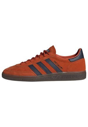 Sneaker basse en daim orange avec des rayures noires, une semelle marron texturée et un marquage "SPEZIAL" sur le côté.
