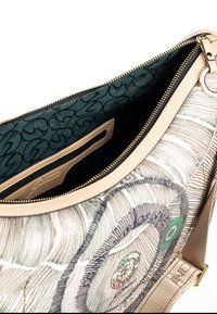 Bolso de textil con ribete de cuero beig, que presenta un patrón circular en colores suaves. Interior forrado con tela verde, incluye un bolsillo con cremallera.