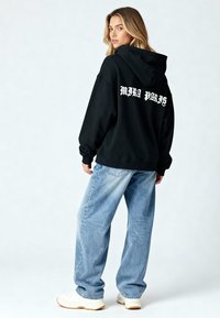 Felpa nera oversize con la scritta "MIRA PARIS" stampata in bianco sul retro. Abbinata a jeans baggy azzurri e sneakers bianche.