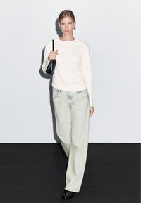 Bílá košile s dlouhým rukávem doplněná světlými džínami s širokými nohavicemi. Černá kabelka a černé boty. Čisté linie a minimalistický design.