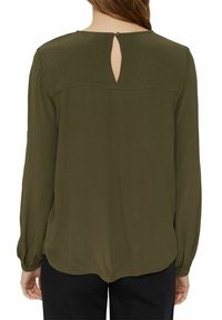 Blusa verde oliva con maniche lunghe, apertura a buco della chiave sul retro e orlo arrotondato. Tessuto morbido e leggero con una sottile texture.