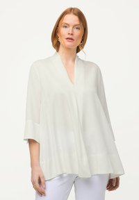 Weiße Bluse mit V-Ausschnitt, Kimono-Ärmeln und fließender Silhouette. Hergestellt aus leichtem, transparentem Stoff. Glatte Textur.