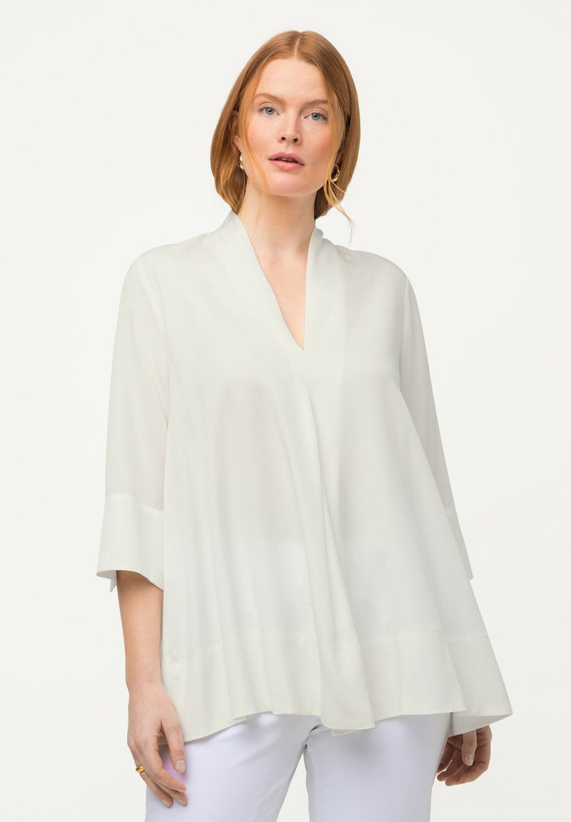 Weiße Bluse mit V-Ausschnitt, Kimono-Ärmeln und fließender Silhouette. Hergestellt aus leichtem, transparentem Stoff. Glatte Textur.