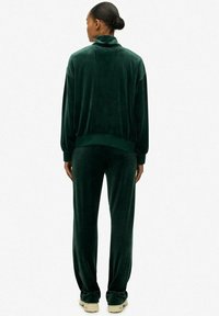 Groene fluwelen trainingspak met lange mouwen, hoge kraag en geribbelde manchetten. Tapered broek met een zachte, gladde textuur.