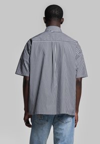 Camicia a maniche corte a strisce in blu navy e bianco, con colletto strutturato e piega sul retro. Abbinata a jeans in denim azzurro chiaro.