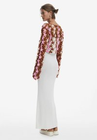 Robe blanche ajustée à manches longues ornée d'appliqués en fleurs marron et rose. Texture lisse avec un subtil éclat ; longueur cheville avec un col rond.