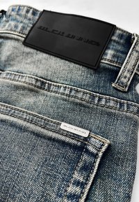 Denim jeans in een vervaagde blauwe kleur met een zwart leren taillebandlabel en een zilveren logo-tag op de achterzak. Zichtbare stikseldetails.