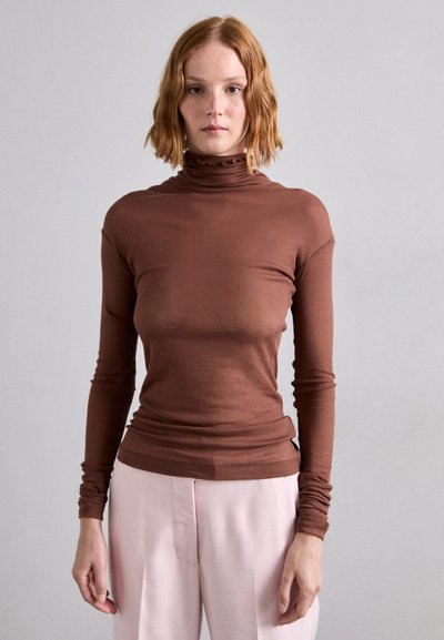 Cămașă braun cu mânecă lungă și guler înalt, cu textură canelată și detalii volan, asortată cu pantaloni roz. Design neted, ajustat.