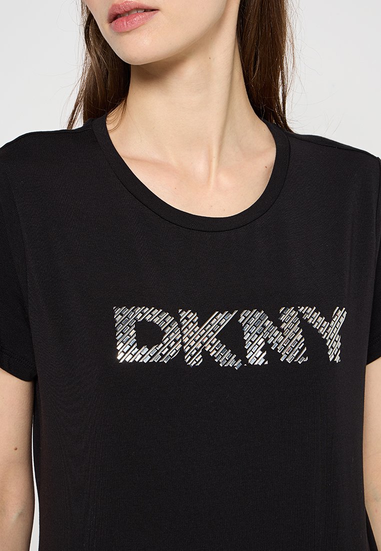 Zwarte korte mouwen t-shirt met een textuur van zilveren "DKNY" logo op de voorkant. De stof lijkt zacht en glad te zijn.