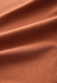 Gestructureerde stof in een warme terracotta oranje kleur, met zachte plooien en een subtiel geribbeld patroon over het oppervlak.