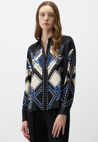 Seidenschirt mit schwarzem Grund und geometrischen Mustern in Blau und Creme, Knopfverschluss und langen Ärmeln mit Manschettendetails.