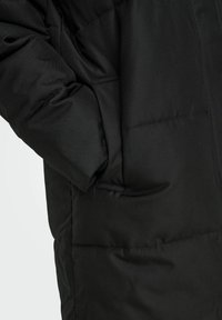 Veste matelassée noire avec une texture lisse, des poches latérales et un design légèrement rembourré, mettant en avant chaleur pratique et protection.