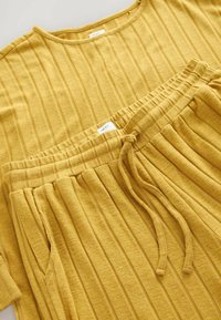 Gul räfflad lounge-set som består av en kortärmad topp och byxor med elastiskt midjeband och snörning. Mjukt, texturerat tyg genomgående.