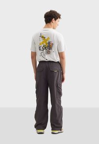 Grå cargobyxor med flera fickor, i kombination med en gräddfärgad t-shirt som har en färgglad grafikdesign och text på baksidan.