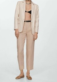 Béžový lněný blazer přes černý bralet, spárovaný s béžovými kalhotami s vysokým pasem a hnědými tkanými slip-on botami, doplněný stříbrným náhrdelníkem.