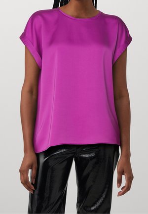Fuchsia kortemouwtop met een ronde hals en een gladde textuur, voorzien van opgerolde mouwen en een ontspannen pasvorm. Gecombineerd met glanzende zwarte broeken.