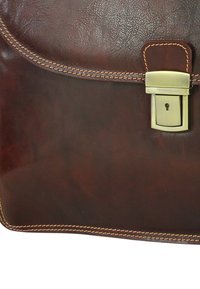 Bruine leren aktetas met een gladde textuur, contrasterende oranje stiksels en een metalen sluiting met een sleutelgatdetail.