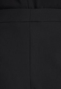 Gros plan sur un tissu noir avec des coutures verticales et horizontales visibles formant un motif en croix.