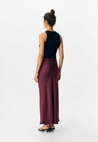 Top nero senza maniche abbinato a una lunga gonna di satin bordeaux fluida. La gonna ha una texture liscia e una silhouette leggermente svasata.