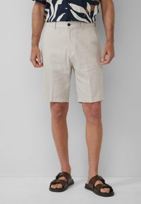 Beige Leinen-Cargo-Shorts mit flachem Bund und Seitentaschen, in entspannter Passform und glatter Textur. Getragen mit braunen Riemchensandalen.