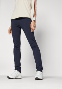 Marina idrottsleggings med en slät textur och fitted design, kombinerat med vita sneakers. Har kontrasterande randiga accenter på tröjan.