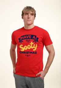 Rød bomuldstrøje med et dristigt, farverigt grafisk design med teksten "HAVE A Sooty CHRISTMAS" og julestemte illustrationer.
