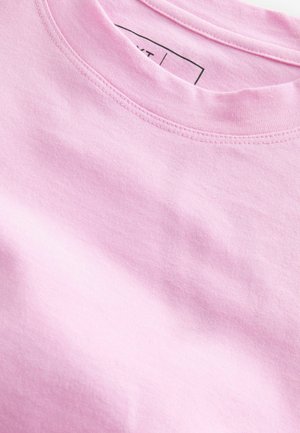 T-shirt en coton rose clair avec un col rond, présentant des coutures fines et une texture douce, partiellement replié pour montrer la qualité du tissu.