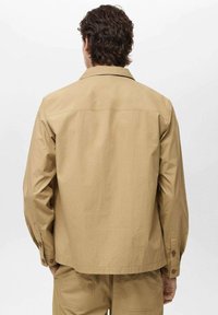 Kaki Utility-Jacke mit Kragen, langen Ärmeln und Knopfdetails. Hergestellt aus einem leichten Stoff, verfügt sie über eine lockere Passform und ein einfaches Design.