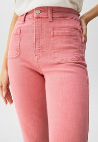 Jean en denim rose avec taille haute, coupe slim et design à cinq poches ; le tissu a une légère texture et des détails de couture visibles.