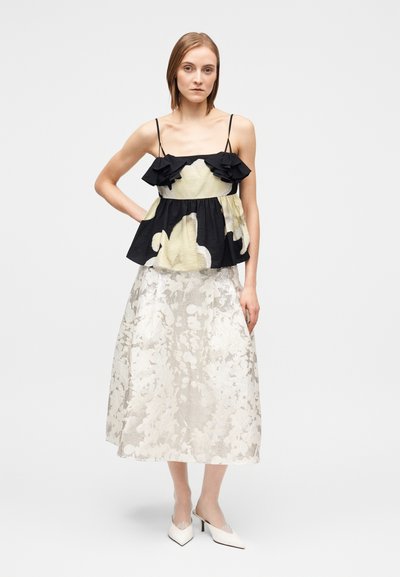 Μαύρο και κρεμ τοπ με φλοράλ σχέδιο και βολάν στις τιράντες, σε συνδυασμό με φούστα σε απαλό χρώμα, με υφή και φλοράλ μοτίβο, και λευκά ψηλοτάκουνα με μυτερή μύτη.