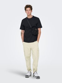 Sort t-shirt med korte ærmer, beige cargobukser med lommer og sorte og hvide sneakers. Lille sort crossbody-taske med justerbar rem.