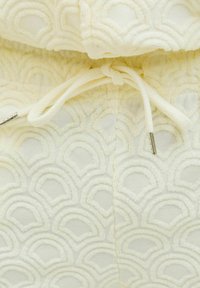 Tela blanca texturada con un patrón de olas en relieve, que cuenta con un cierre de cordón con terminales de metal.
