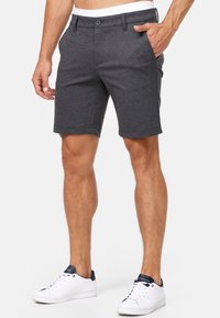 Shorts gris en tissu doux, avec fermeture à bouton, deux poches latérales et coupe droite. Portés avec des baskets blanches.