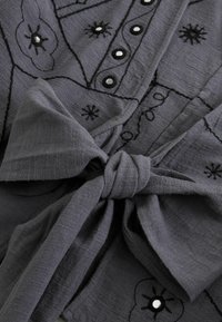 Dark gray fabric with black embroidered floral patterns and round reflective beads, tied in a knot.