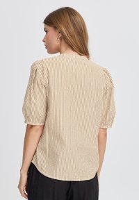 Beige og brun stribet skjorte med pufærmer, rund halsudskæring og en let buet kant. Fremstillet af letvægts, struktureret stof.