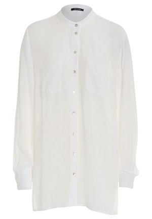 Chemise blanche à manches longues et à boutonnières, fabriquée dans un tissu léger et texturé. Présente un col montant et deux poches avant. Boutons argentés.