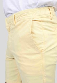 Shorts en coton jaune avec une texture lisse, arborant des poches latérales et une coupe ajustée. Ceinture élastique pour le confort et un enfilage facile.