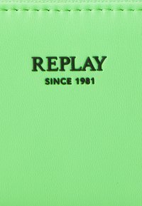 Zielony portfel z syntetycznego materiału o teksturowanym wykończeniu; z wytłoczonym logo "REPLAY" oraz napisem "SINCE 1981" w kolorze czarnym. Kompaktowy, prostokątny kształt.