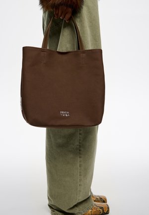 Bruine tote bag met een gladde textuur, voorzien van gestikte randen en twee stevige handvatten. Het "BIMBA Y LOLA" logo is ingedrukt aan de onderkant van de voorkant.