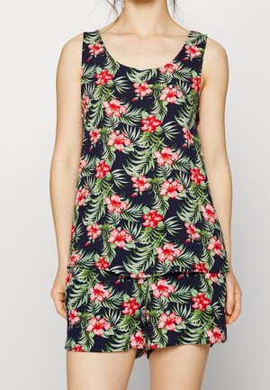 Ærmeløs mørkeblå top og matchende shorts med grønt blad- og rødt hibiscusblomsterprint båret af en person.