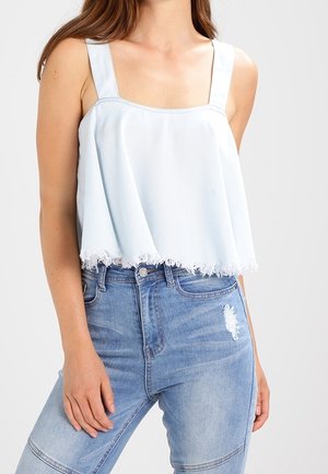 Top corto azul claro con tirantes anchos, escote cuadrado y dobladillo deshilachado. Combinado con jeans claros de mezclilla desgastados.